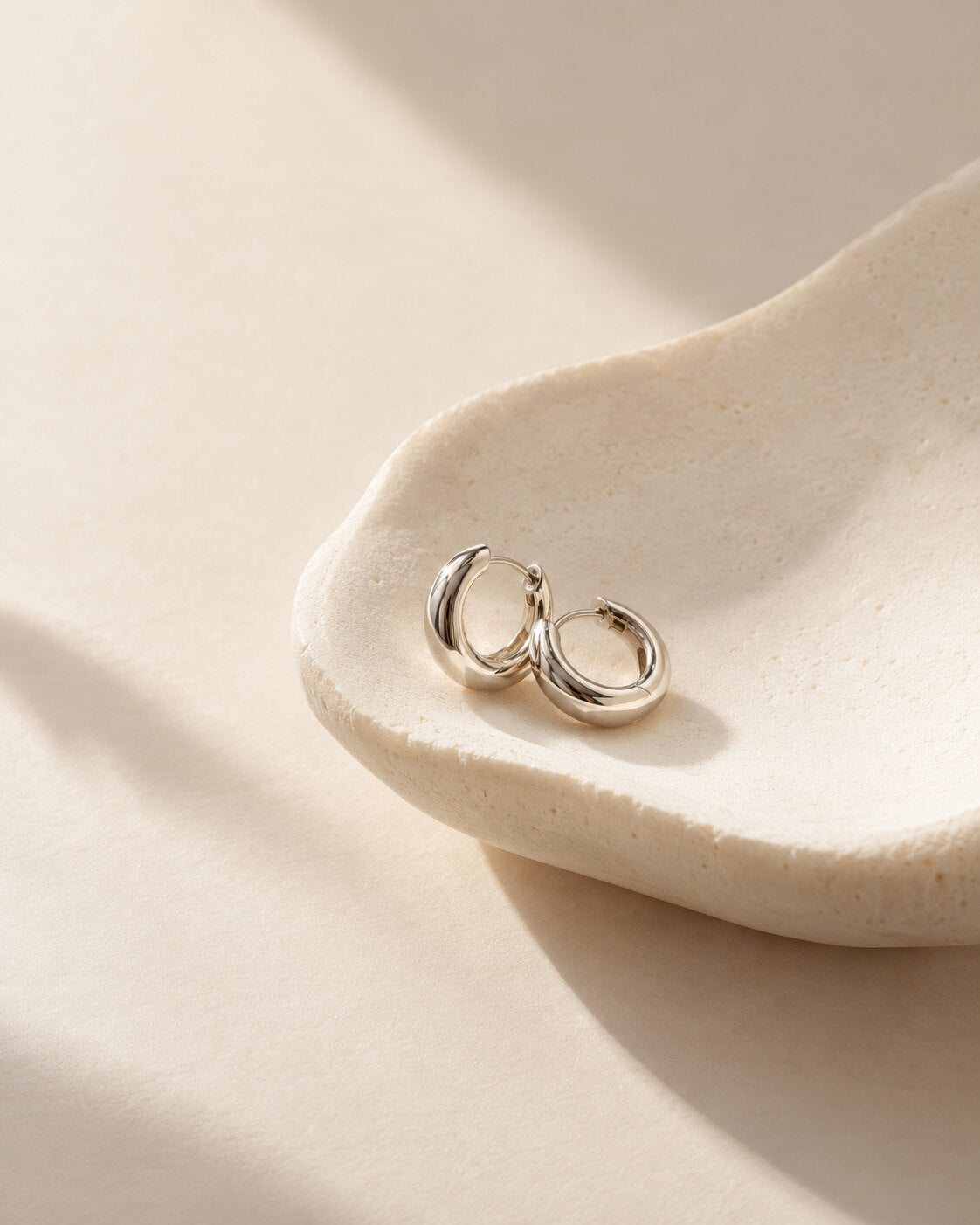 Silver hoop earring-inspired editorial still life on an alabaster form